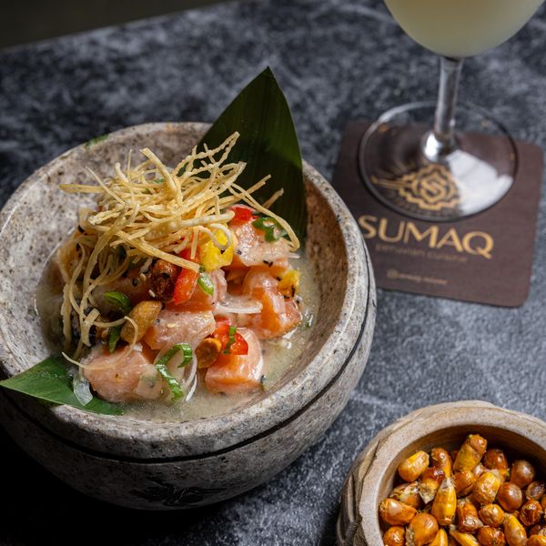 A vibrant ceviche dish with crispy toppings and a cocktail. Sumaq Miami restaurant.