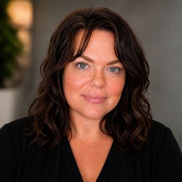 Woman with dark wavy hair and blue eyes smiling gently.