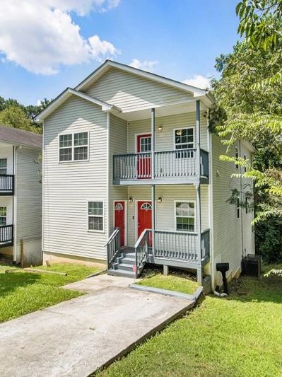 Two-story duplex with red doors and balconies, surrounded by greenery.