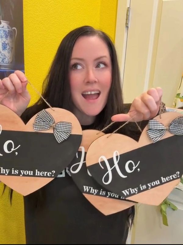 Woman holding heart-shaped signs saying, "Ho, Why is you here?"