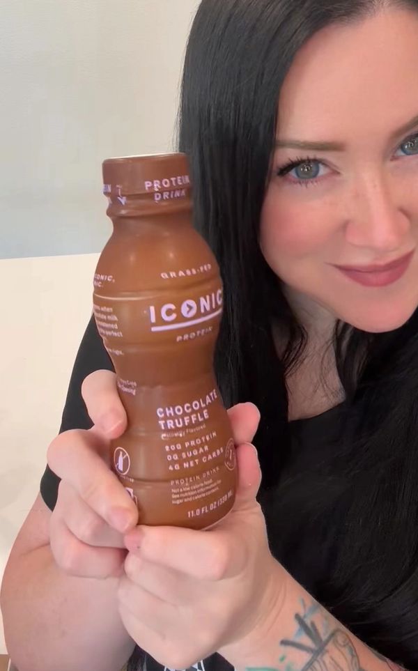 Smiling woman holding a chocolate truffle protein drink bottle.