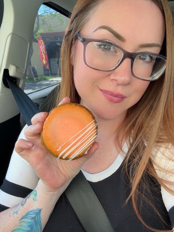 Woman with glasses holding an orange dessert in a car.