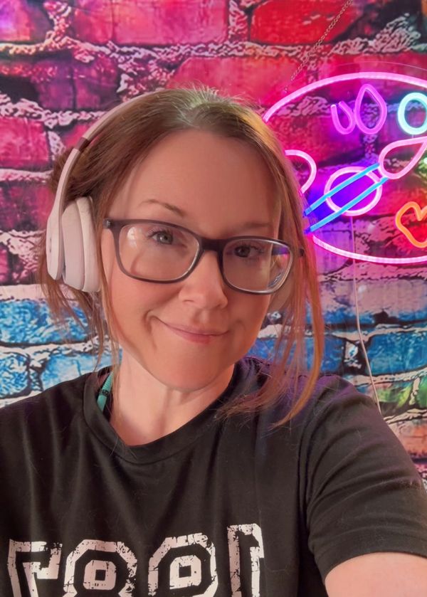 Woman smiling with headphones in front of colorful neon art wall.