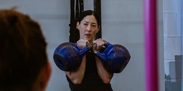 Woman lifting two kettlebells in a gym during a workout.