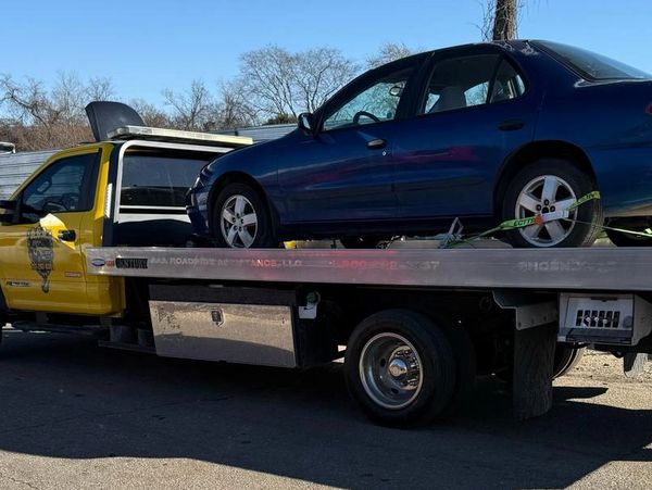 A blue car is being towed on a flatbed truck on a clear day.