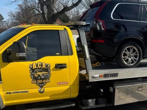 Yellow tow truck carrying a black SUV on a sunny day.