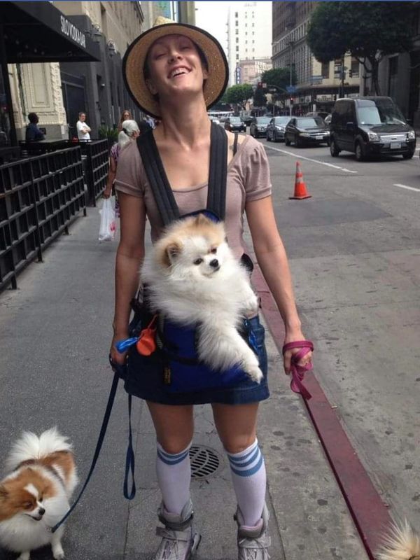 Woman walking with two fluffy dogs, one in a carrier and one on a leash.