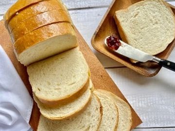 Freshly sliced white bread on wooden boards with butter and jam spreader.