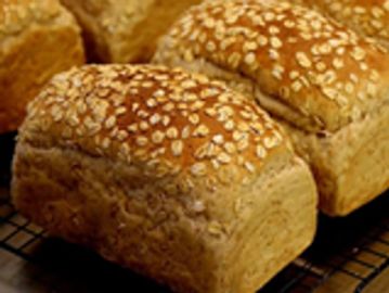 Freshly baked oat-topped bread loaves cooling on a rack.