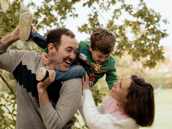 A joyful family moment with parents playing and laughing with their child outdoors.