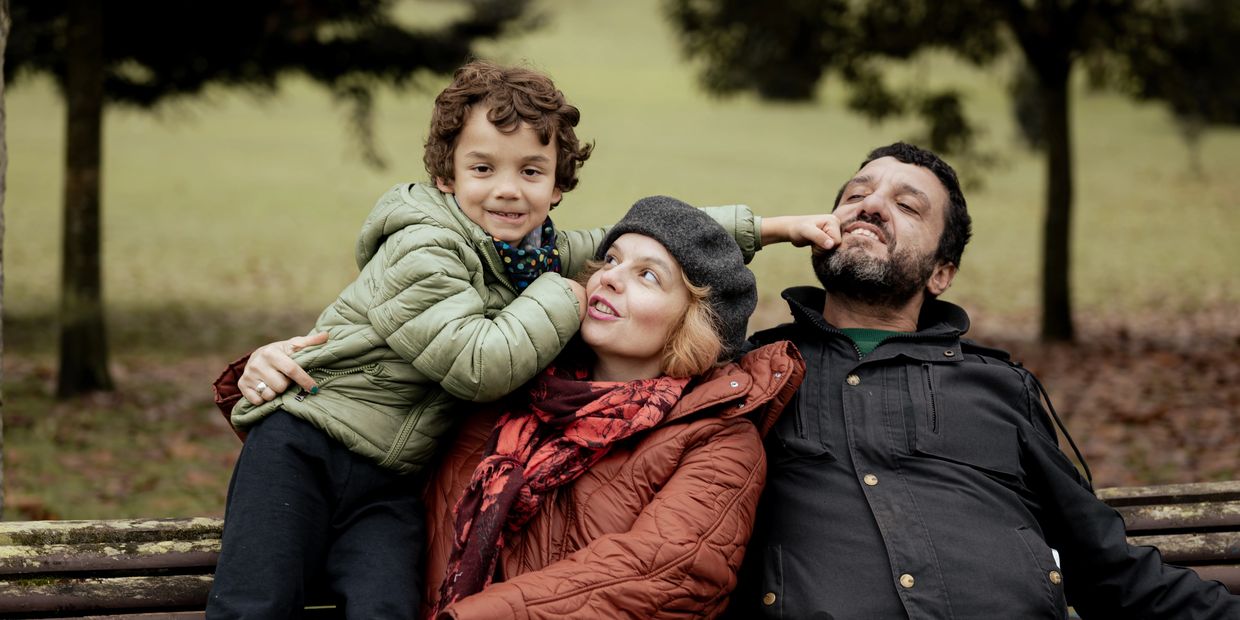 A child playfully punches a man while sitting with a woman on a park bench.