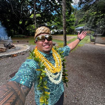Man wearing leis and sunglasses, smiling outdoors.