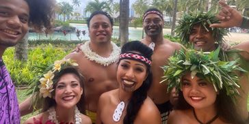 Group of people in traditional Polynesian attire smiling outdoors.