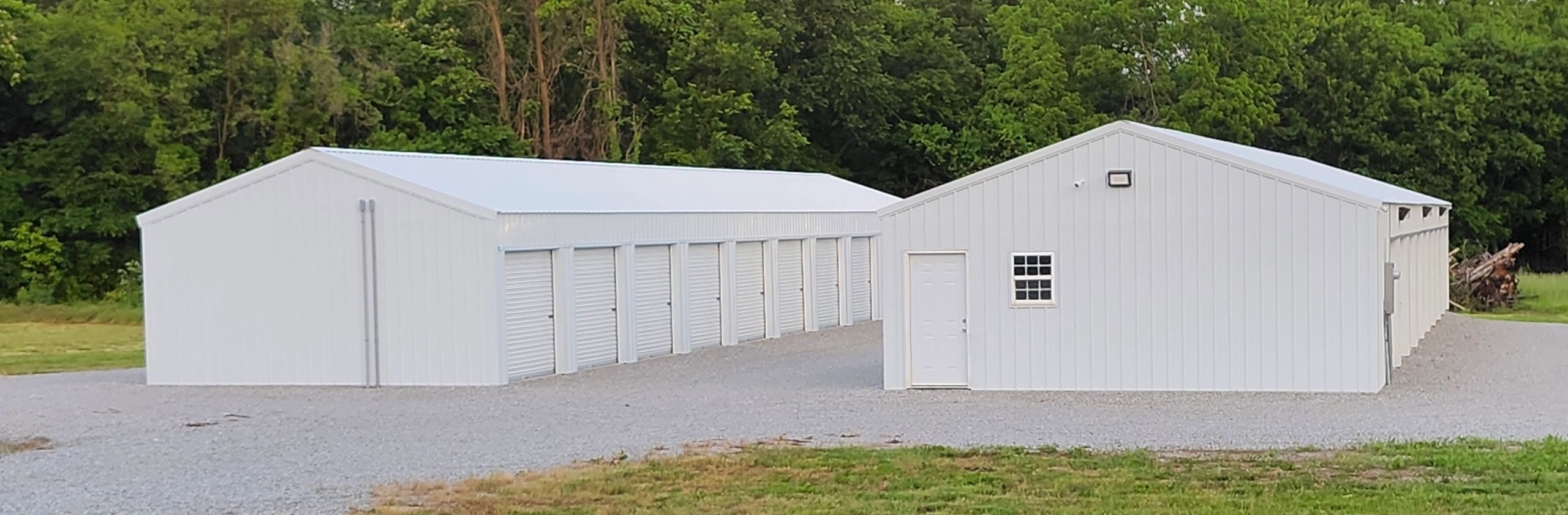 Two white storage buildings with multiple roll-up doors in a green outdoor setting.