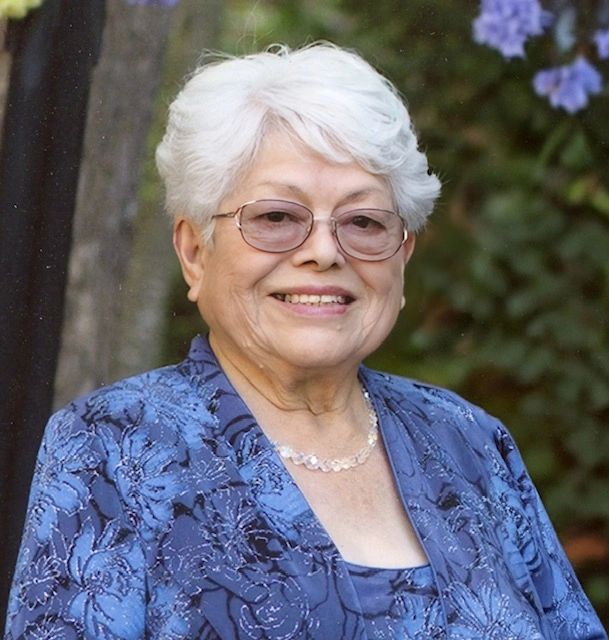 Elderly woman with white hair and glasses smiling warmly.