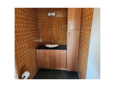 Bathroom vanity with wood cabinets, tile walls, and black countertop