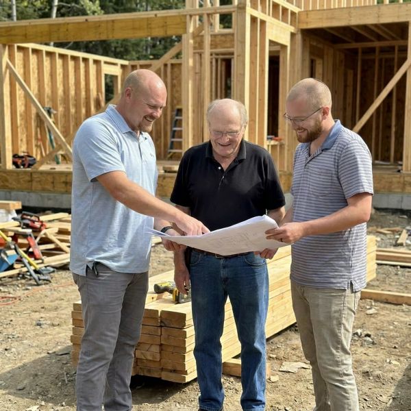 Three men discussing blueprint at construction site.