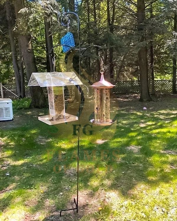 Two bird feeders hanging on a metal pole in a backyard.