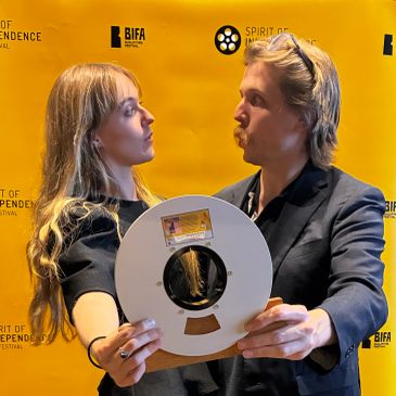 Two people holding a round award at a film festival.