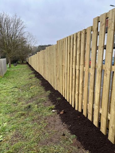 New wooden fence alongside a grassy path with fresh soil.