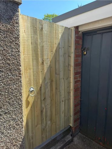 New wooden fence panel next to a brick and concrete wall.
