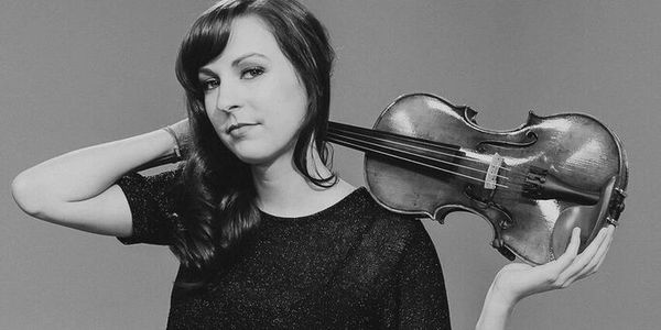 Woman posing with a violin resting on her shoulder in a black-and-white photo.