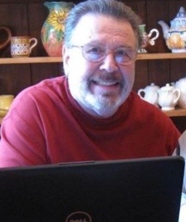 Smiling man in glasses and red sweater using a Dell laptop in a cozy kitchen.