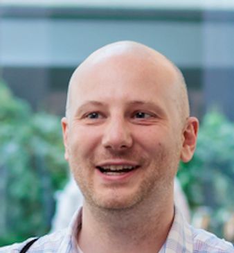 Smiling bald man in a casual shirt with blurred background.