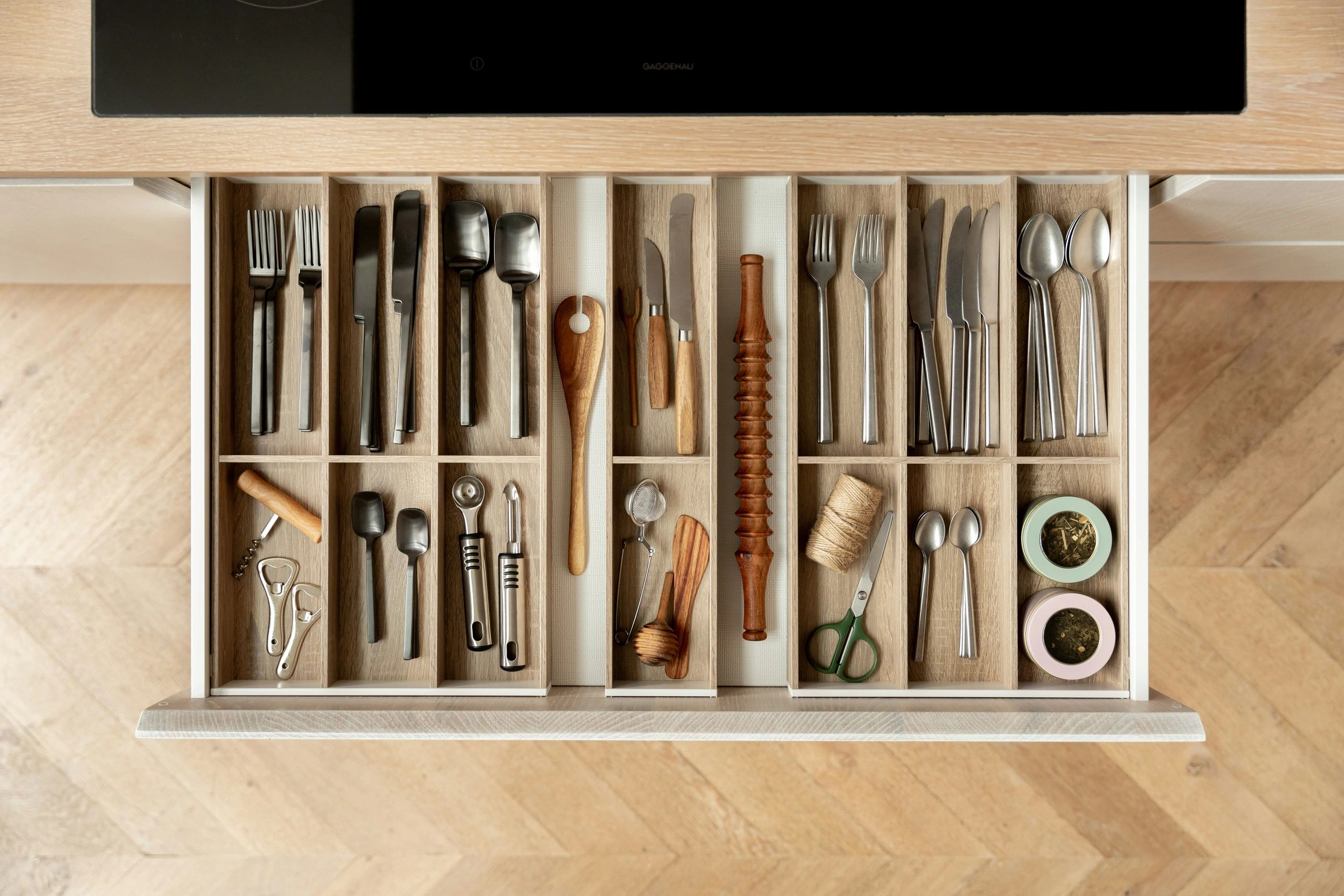 Organized kitchen drawer with utensils and tools in wooden compartments.