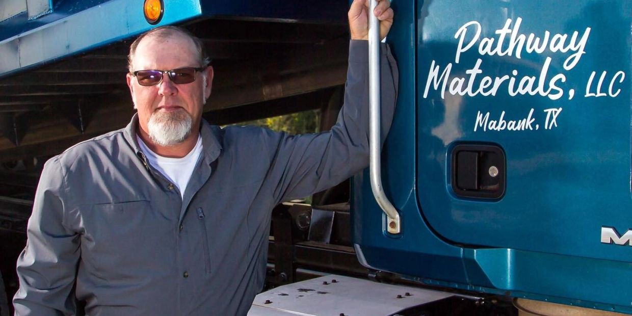 Man in sunglasses leaning on a blue Pathway Materials truck in Mabank, TX.
