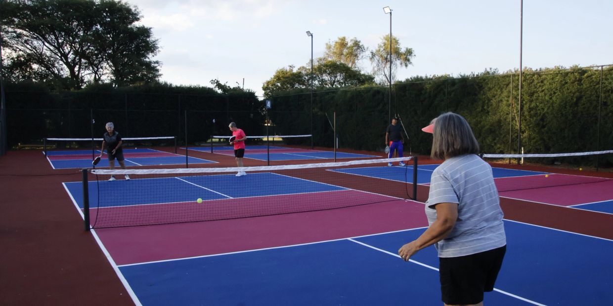 Four people playing pickleball on colorful courts outdoors.