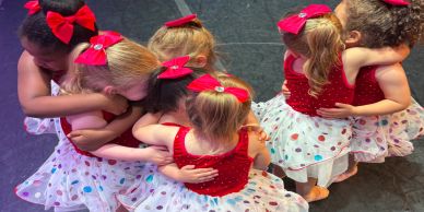 Young girls in dance costumes hugging in a group.