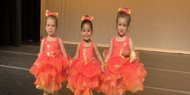 Three young girls in orange tutus on stage.