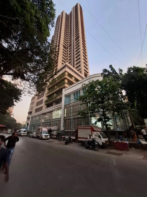 Tall building with parked vehicles and trees on a street.