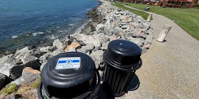 Fishing trash bins on a rocky waterfront path.