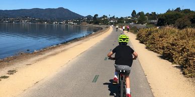 Child riding bike on scenic waterfront path.