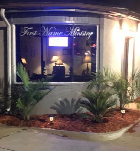 Night view of First Name Ministry building with indoor lamps and outdoor plants.