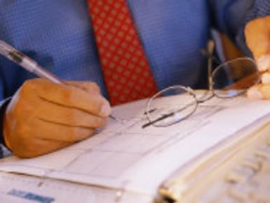 Close-up of hands writing in a binder, glasses nearby.