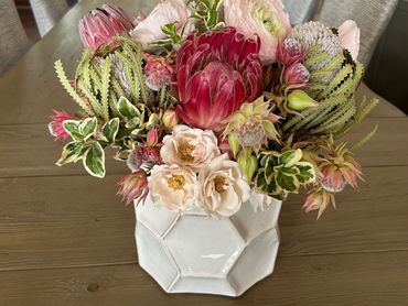 Elegant floral arrangement in a white geometric vase on a wooden dining table.