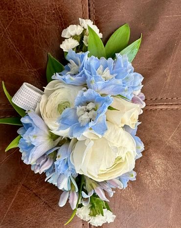 Delicate blue and white floral corsage with green leaves.