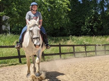 A rider is trotting towards the camera on a big gray horse.