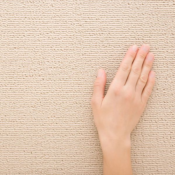 Hand touching a beige textured carpet surface.