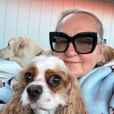 Woman with large black glasses posing with two dogs, one close-up.