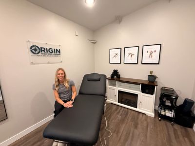 Woman sitting in a modern therapy room with a black treatment table.