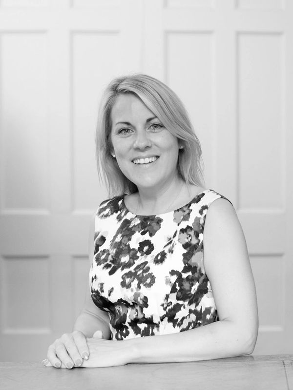 Smiling woman sitting at a table in a floral dress.