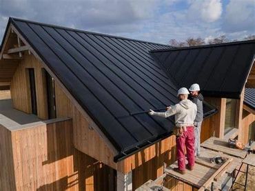 Two construction workers inspecting a black metal roof on a wooden house.