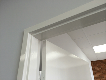Close-up of a white door partially open with a white door frame and ceiling tiles.