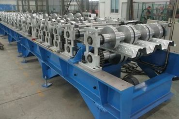 Industrial metal forming machine with rollers on a blue base.