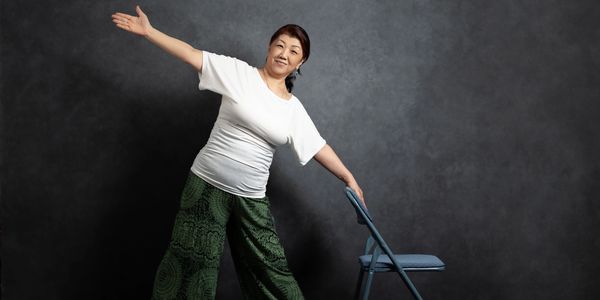 Woman stretching using a chair for support.