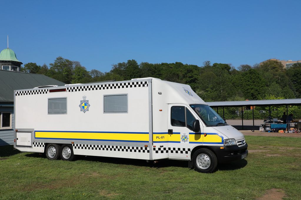 A large white police van with yellow and blue stripes parked on grass.